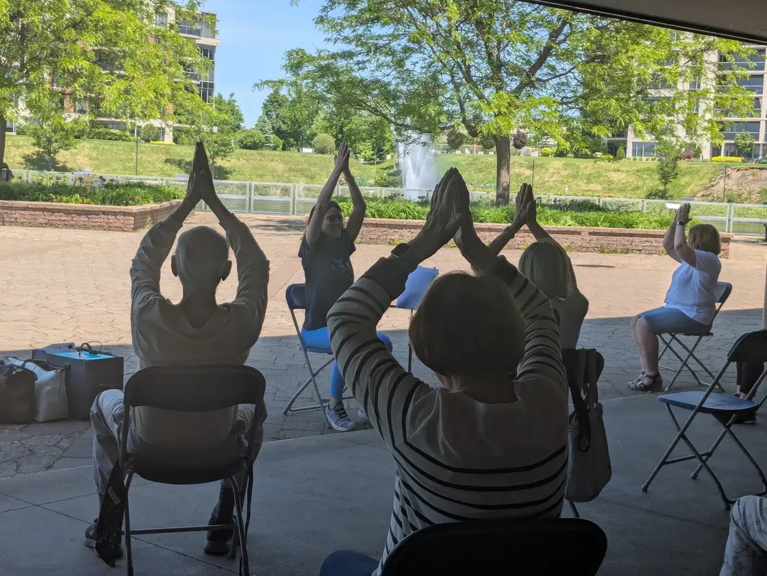 Séance de yoga sur chaise en plein air avec un groupe d’aînés, bras levés